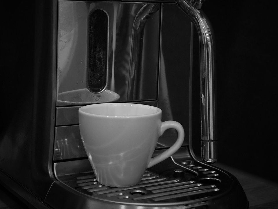 An espresso machine pouring into a white cup in black and white